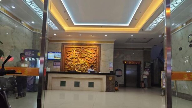 Un vestíbulo de hotel con una recepción, un gran muro decorativo y una pantalla digital.