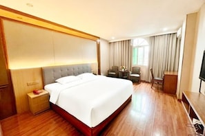 A hotel room with a large bed, a desk, a chair, and a television. - Fengdu Business Hotel (Shishi)