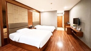 Habitación de hotel con dos camas, suelo de madera, televisor y cabecero de madera.