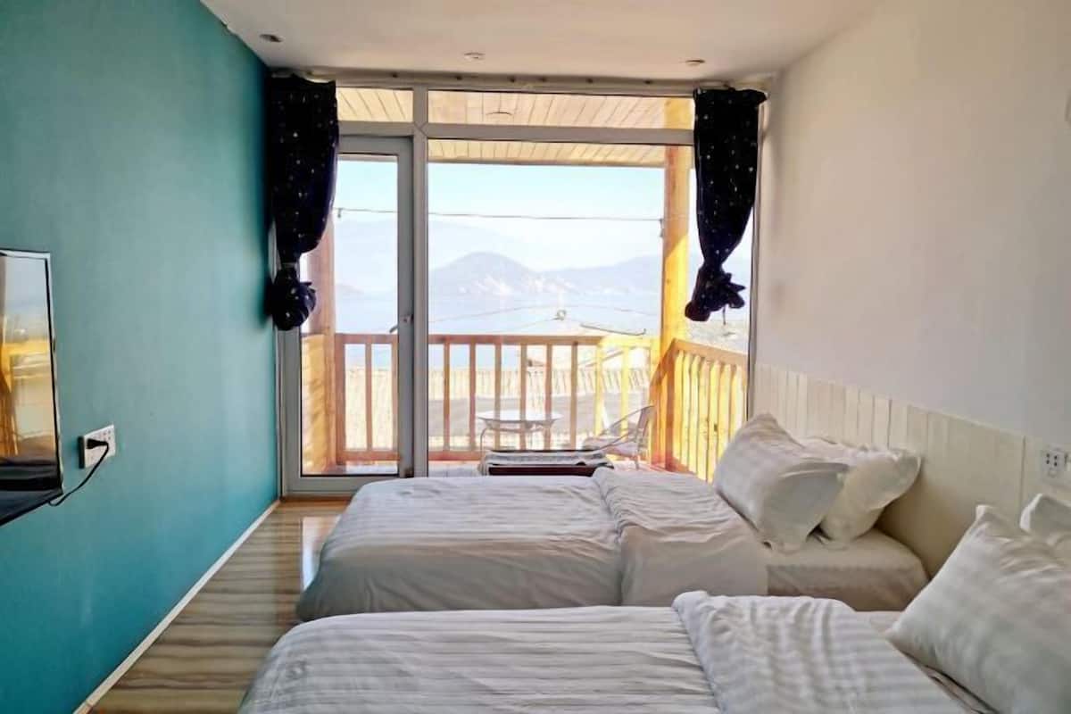 A bedroom with two beds, a TV, and a balcony with a view of mountains.