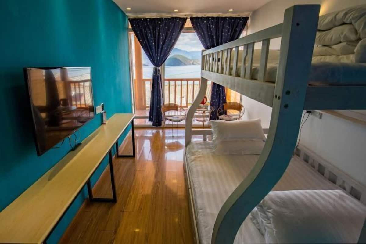 A bunk bed room with a view of the sea, a bench, and a table.