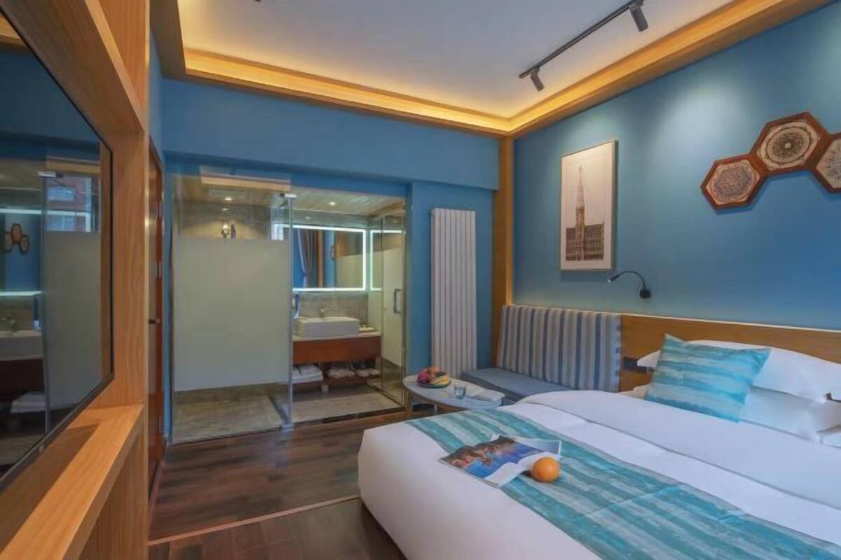 A modern hotel room with a large bed, a bathroom with a glass shower, and a view of the cityscape.