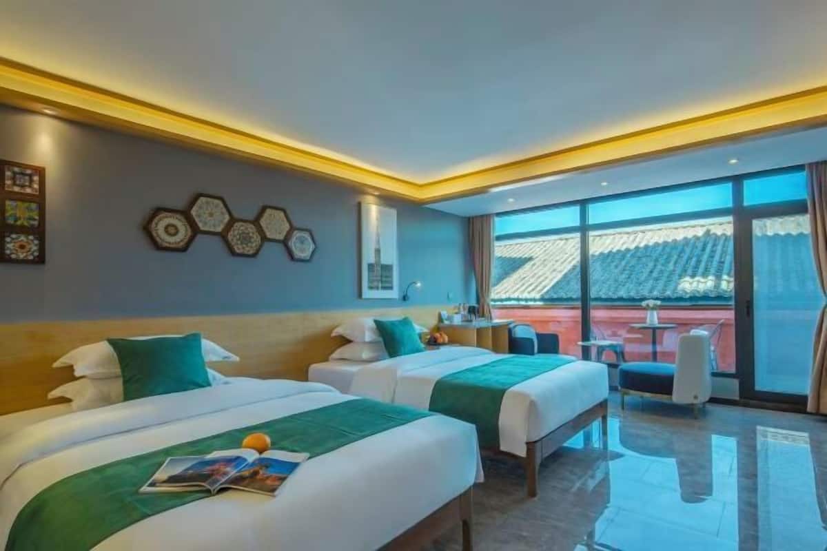 A hotel room with two beds, a desk, and a view of a red-roofed building.