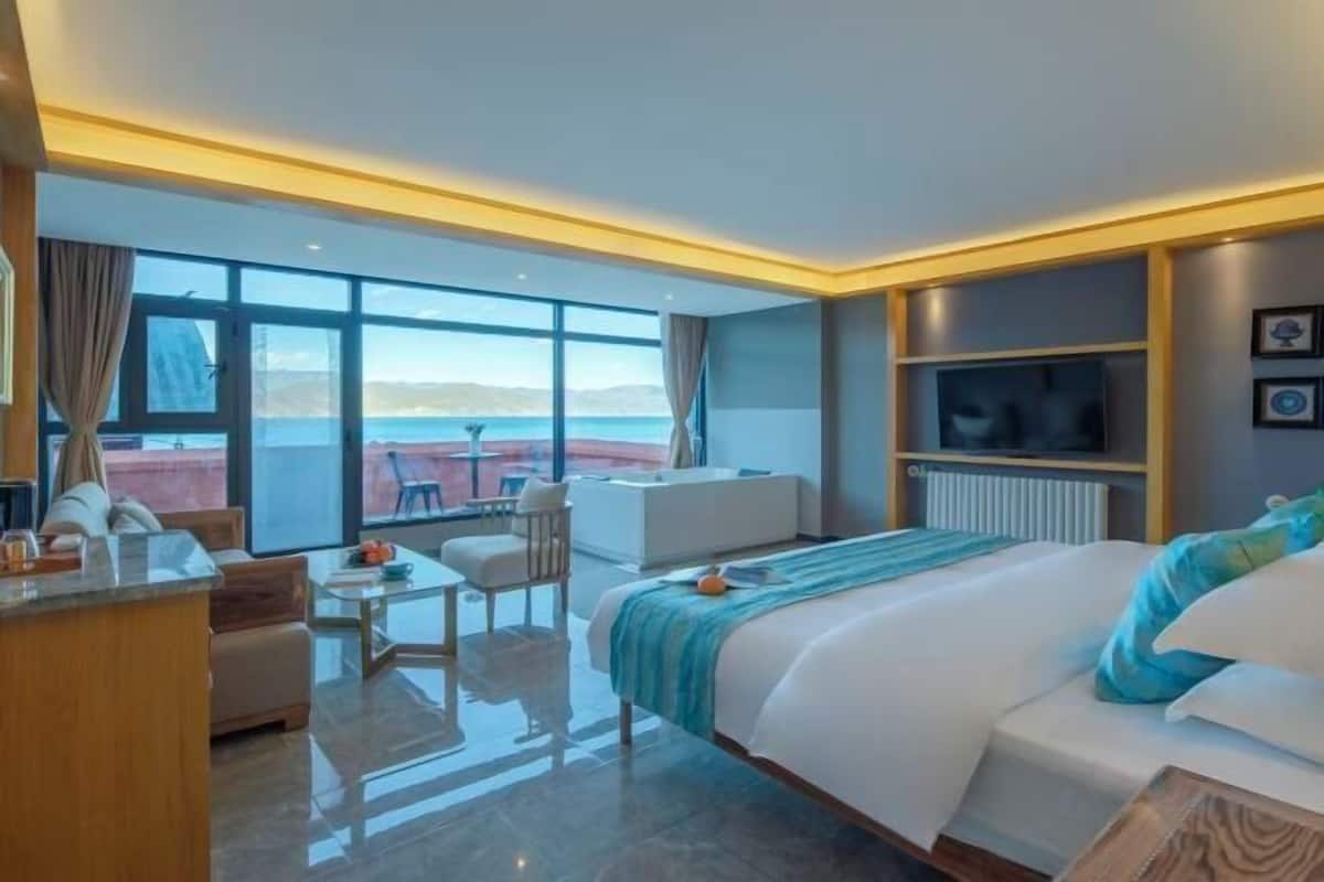A modern hotel room with a large bed, a seating area with a table, and a view of the sea.