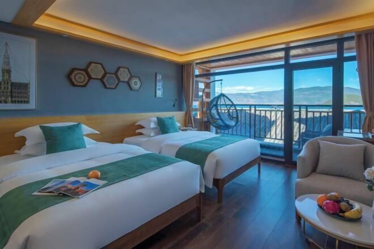 A hotel room with two beds, a balcony with a view, and a dining area with fruit.