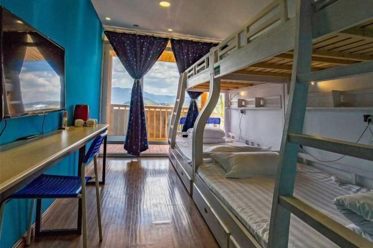 A bunk bed room with a desk and chair, wooden flooring, and curtains.