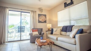A living room with a sofa, a coffee table, a dining area with chairs, a sliding glass door, and a wall-mounted fan.