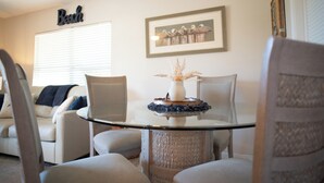 A living room with a glass-top coffee table, a framed picture on the wall, and a word 'Beach' above a window.