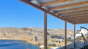 Uma área de estar coberta ao ar livre, com vista para o mar e colinas rochosas.