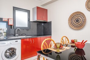 A compact kitchen with a washing machine, a dining table with chairs, and a red cabinet.