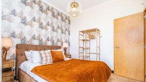 Une chambre à coucher avec un grand lit, une armoire en bois, une table de chevet et un mur orné d’un motif d’arbre.