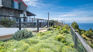 Une maison située sur la côte, avec une façade en pierre, un toit rouge et un balcon donnant sur la mer.