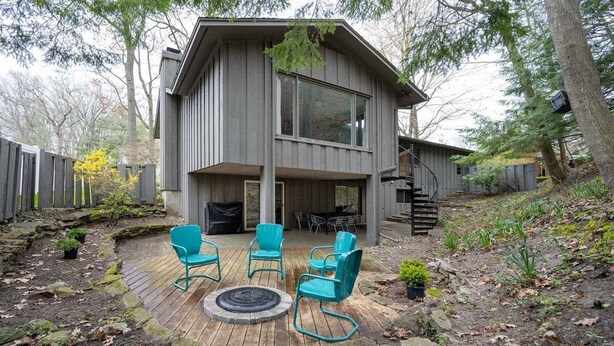 Ein modernes, zweistöckiges Haus mit Terrasse, Sitzgelegenheiten im Freien und einem Feuerkorb.