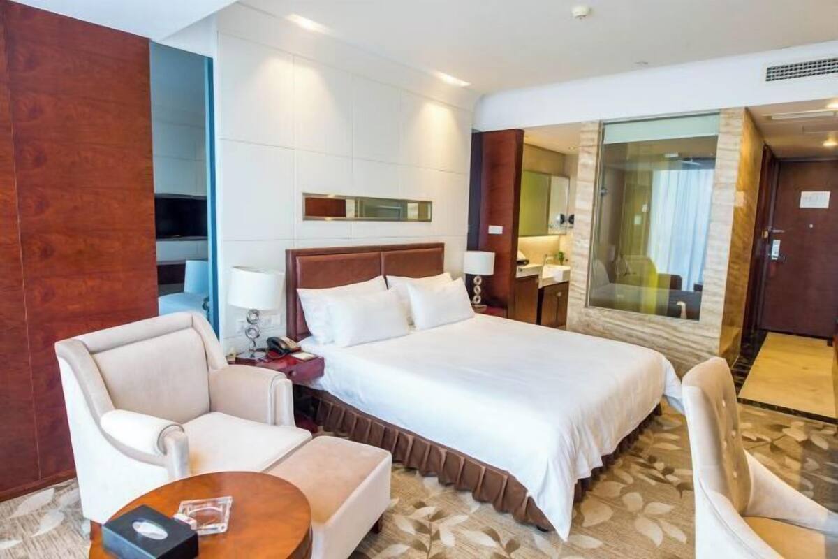 A hotel room with a large bed, two armchairs, a small table, and a mirror.