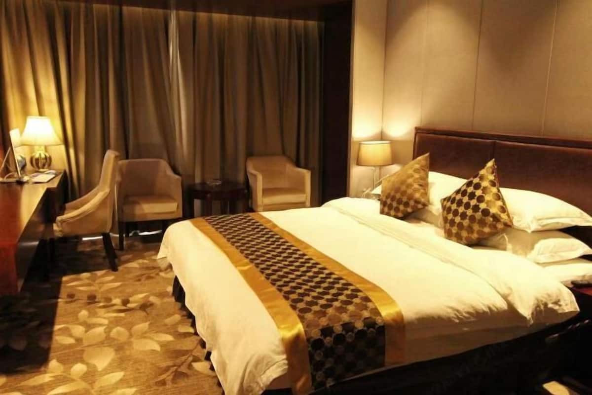 A hotel room with a bed, two armchairs, a small table, and a lamp.