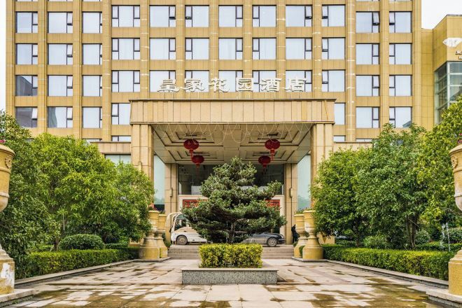 A hotel entrance with a large building facade, a central entrance canopy, and a well-maintained garden area.