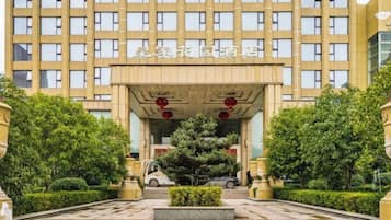 A hotel entrance with a large building facade, a central entrance canopy, and a well-maintained garden area.
