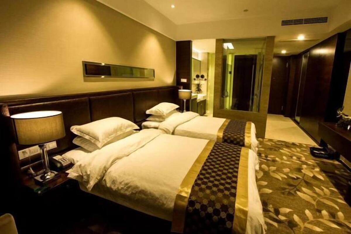 A hotel room with two beds, a bedside table with a lamp, a mirror, and a carpeted floor.