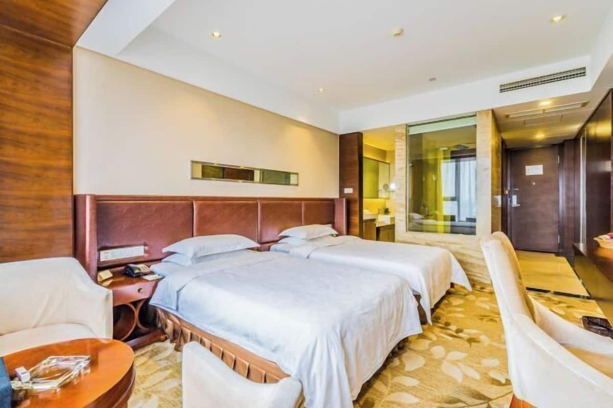 A hotel room with two beds, a sitting area with a sofa, a small table, and a large window.