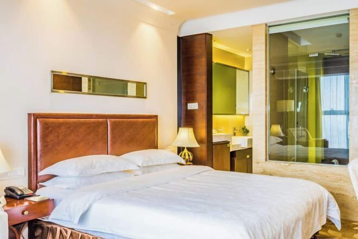 A hotel room with a bed, bedside table, lamp, and a large window.