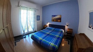Una camera da letto con un letto, una finestra con tende, un quadro appeso al muro e un comodino.