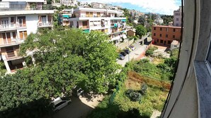 Un quartiere residenziale con edifici a più piani, una strada con auto parcheggiate e un grande albero sullo sfondo.