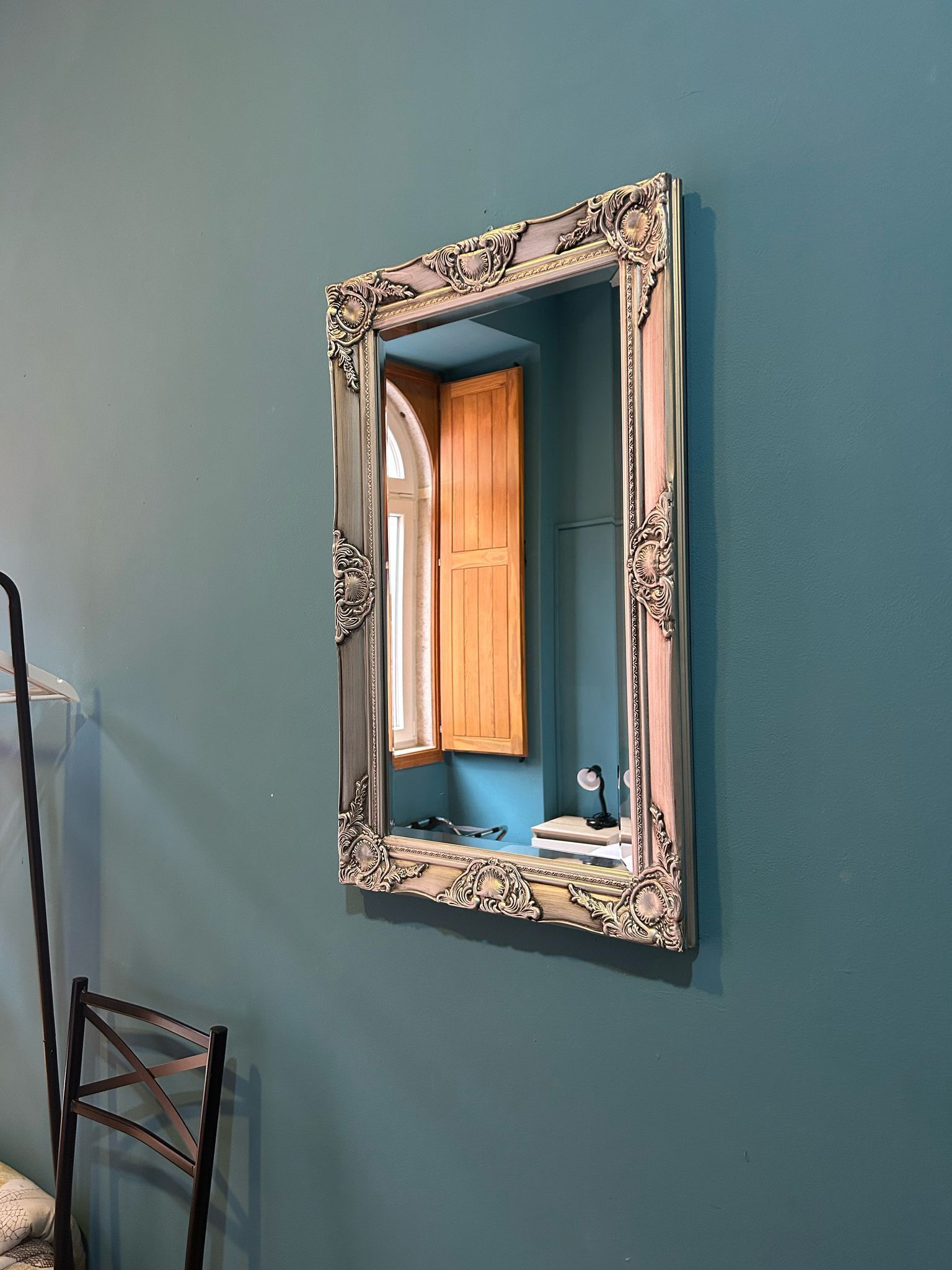 A mirror with an ornate frame mounted on a teal wall.