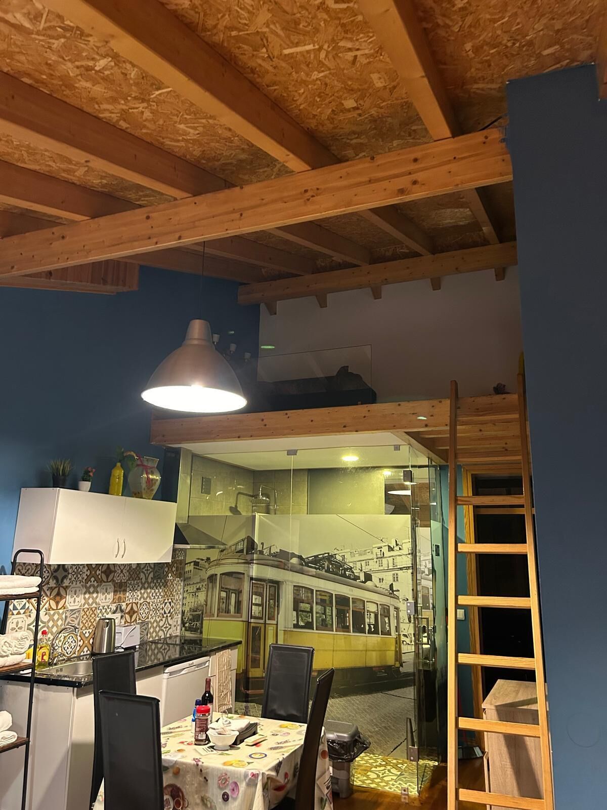 Une pièce comprenant une table à manger, des chaises, un luminaire suspendu et une vue sur un tramway à travers un mur de verre.