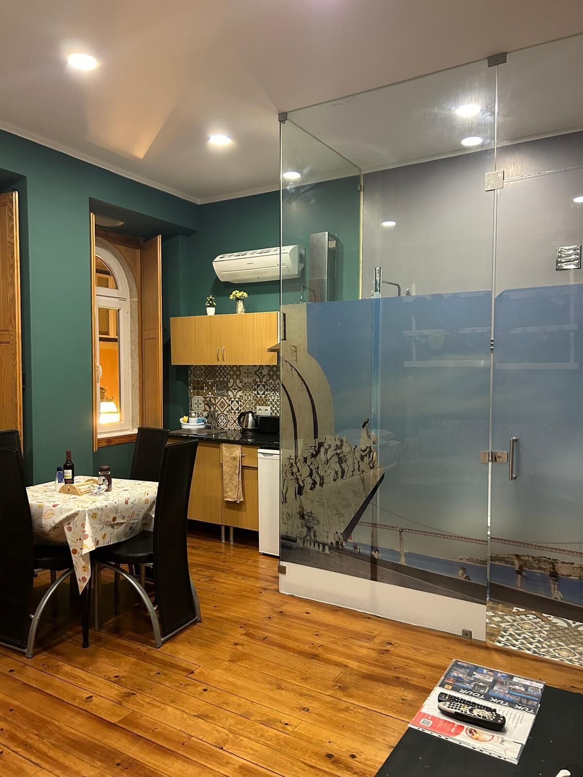 A modern kitchen with a dining area, featuring a wooden table, chairs, and a glass partition with artwork.