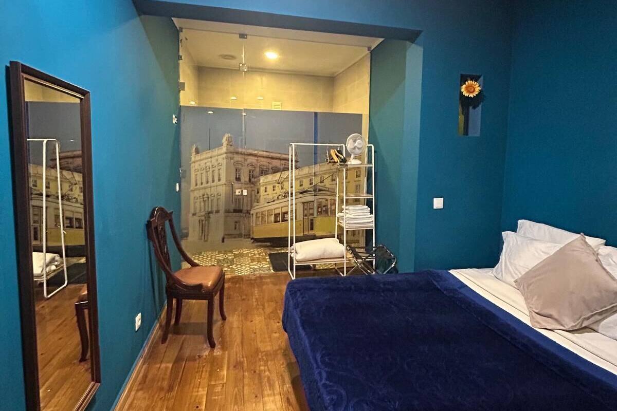 A bedroom with a bed, a chair, a mirror, and a view of a cityscape through a window.