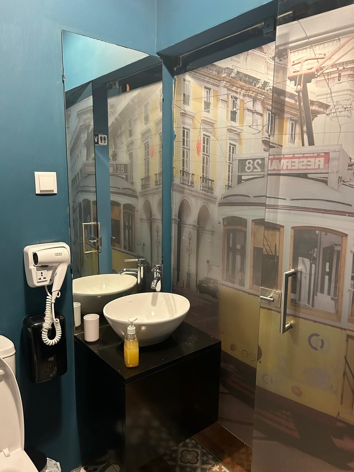 A bathroom with a large mirror, a white sink, a hairdryer, and a bottle of soap.