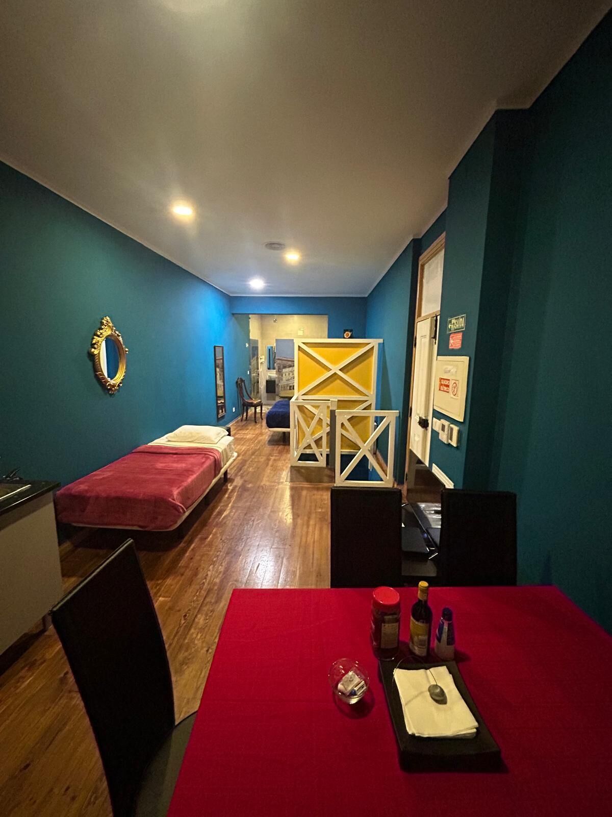 A compact room with two single beds, a small table with a red tablecloth, and a chair.