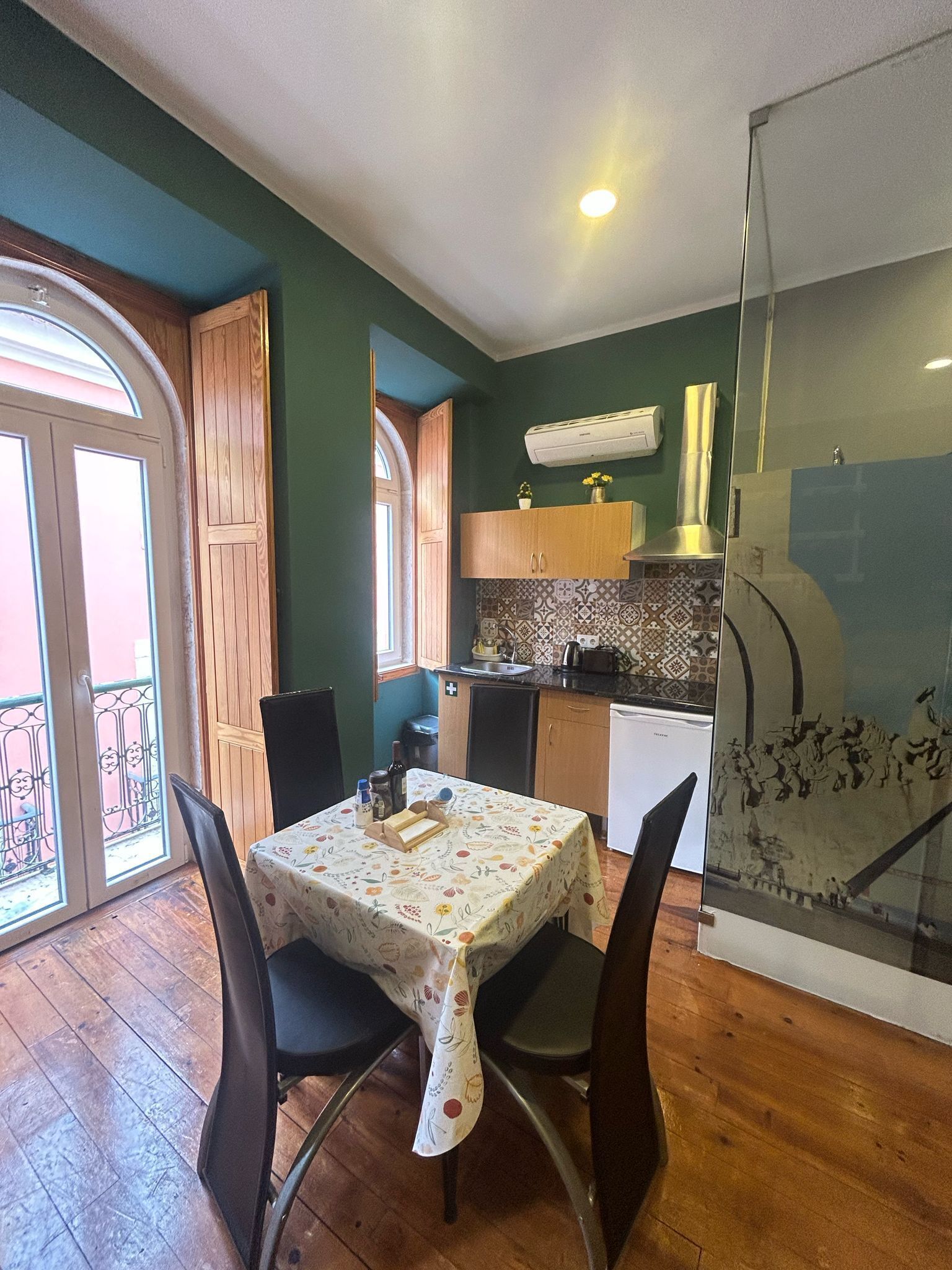 A dining area with a table set for two, a kitchen with wooden cabinets, and a glass door leading to a balcony.