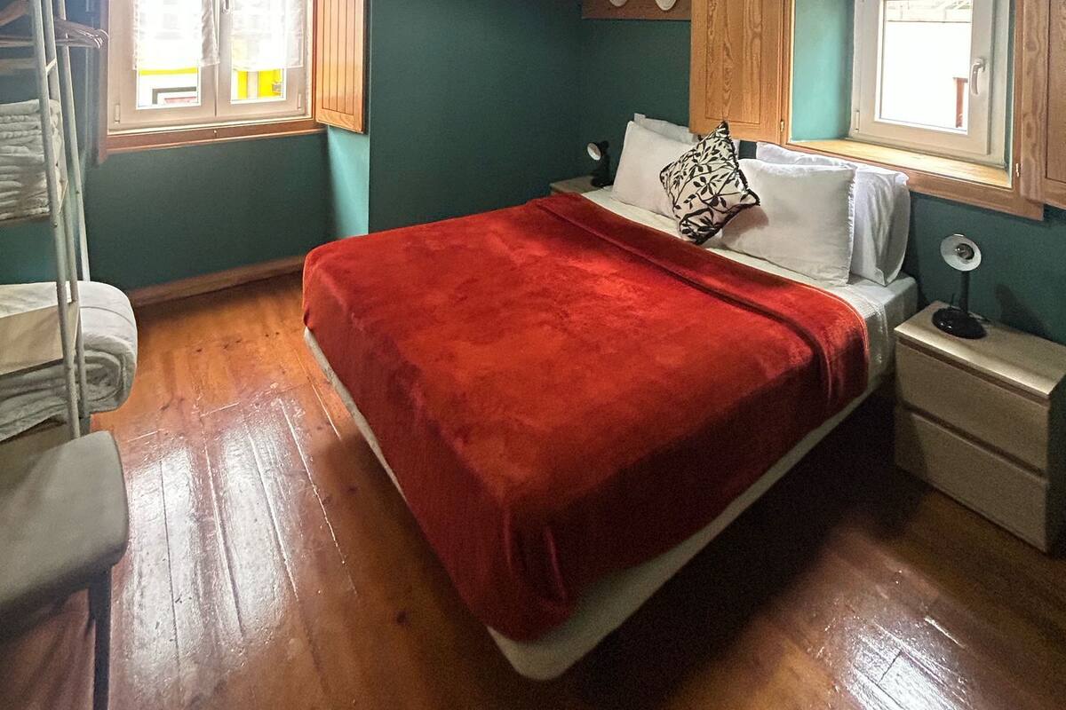 A room with a bed, a window, a ceiling fan, and a wall-mounted air conditioner.