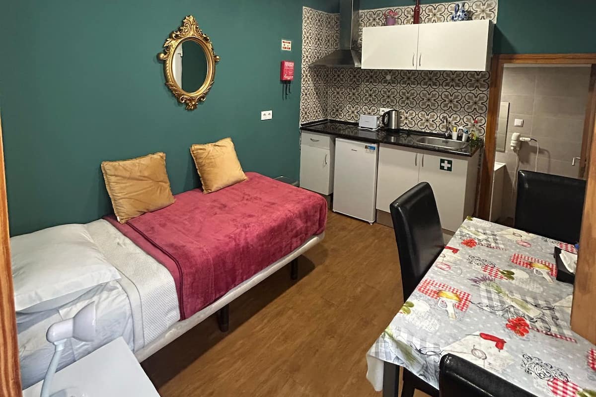 A compact room with a bed, a small kitchenette, a dining table, and a mirror.