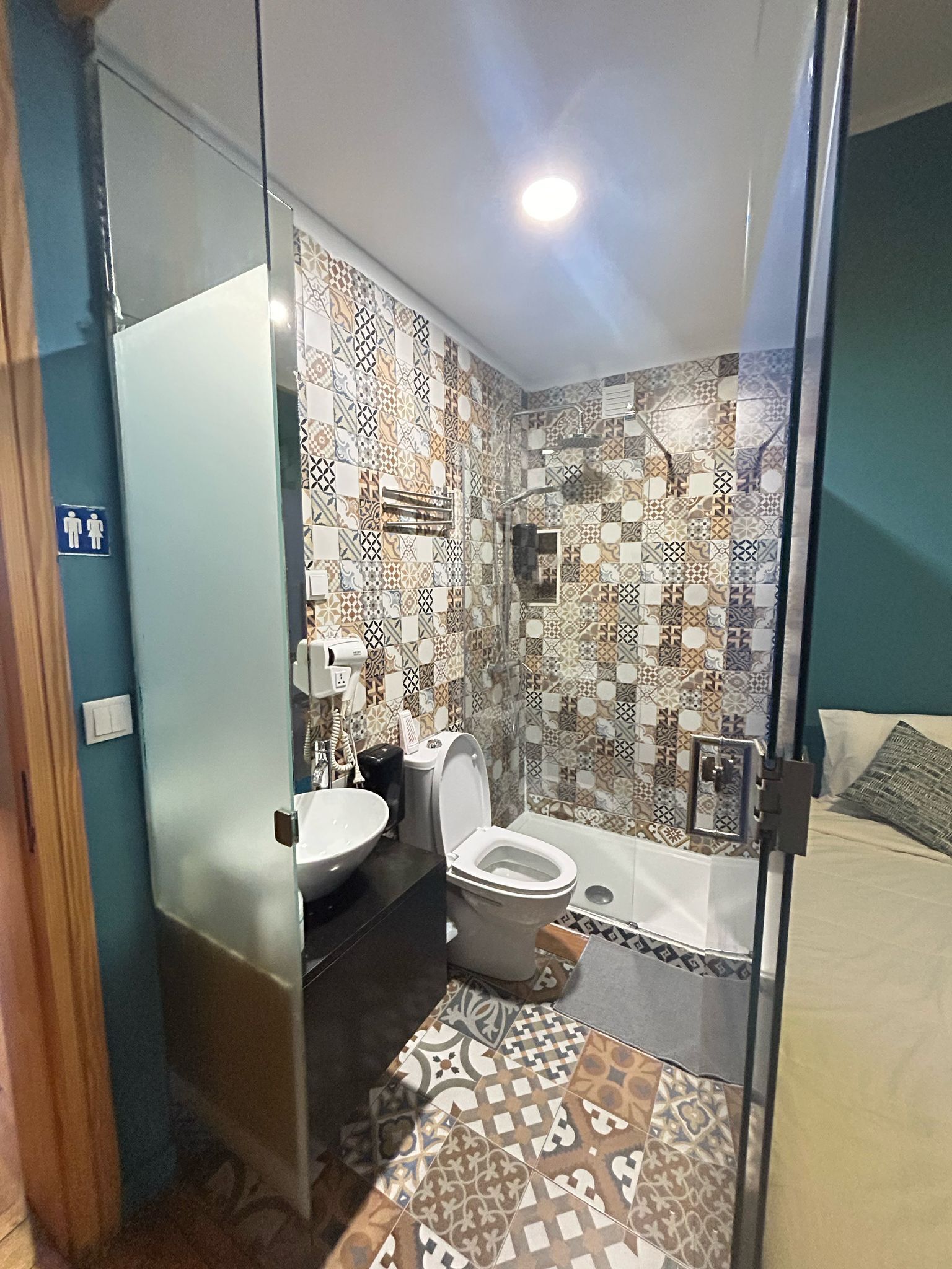 A bathroom with a toilet, sink, and shower. The walls are tiled with a patterned design.