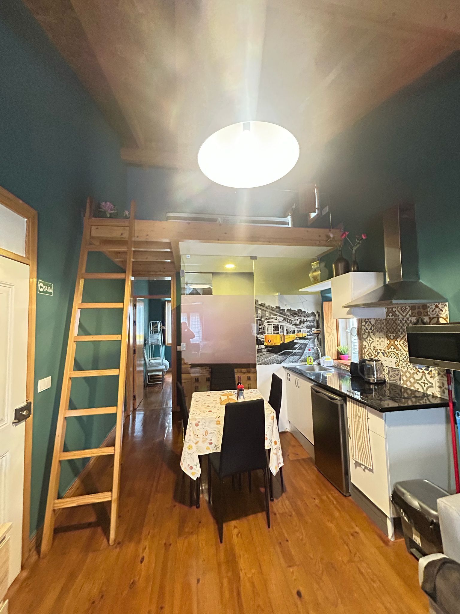 A compact kitchen with a dining area, wooden ladder, and a view of a train.