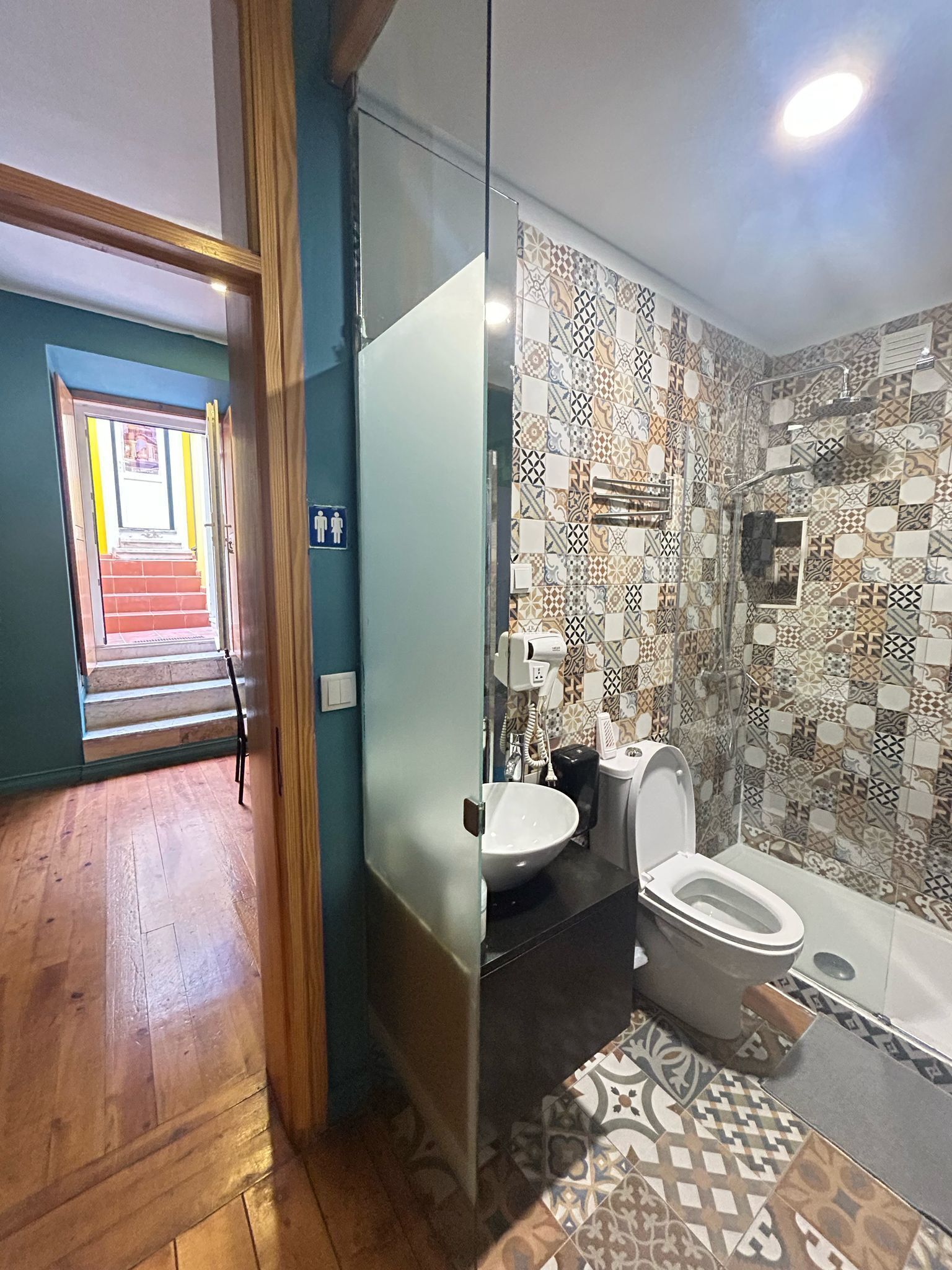A bathroom with a patterned tile wall, a glass shower enclosure, and a wooden floor.