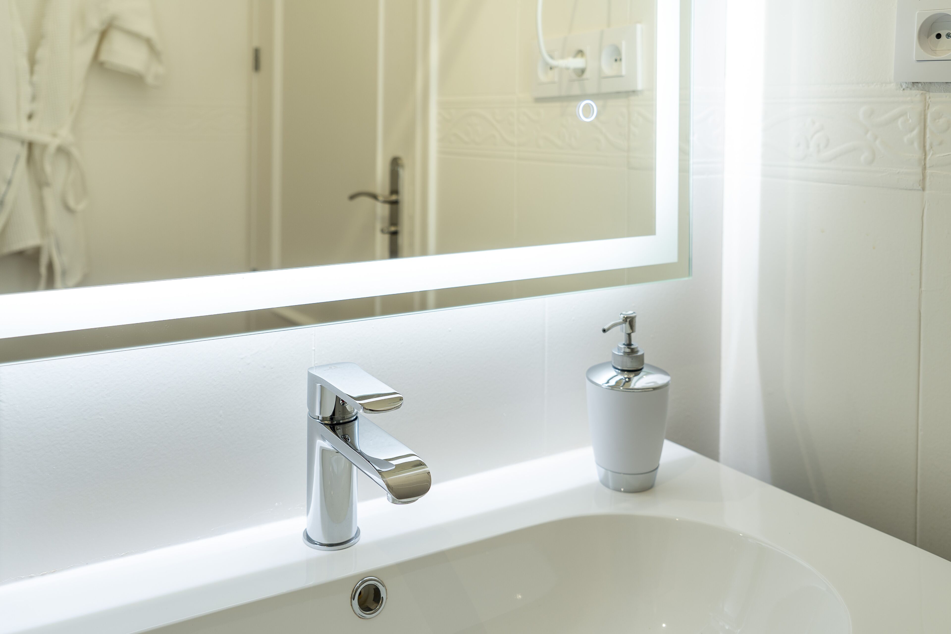 Ein modernes Badezimmer mit einem weißen Waschbecken, einem chromfarbenen Wasserhahn und einer Seifenspender.
