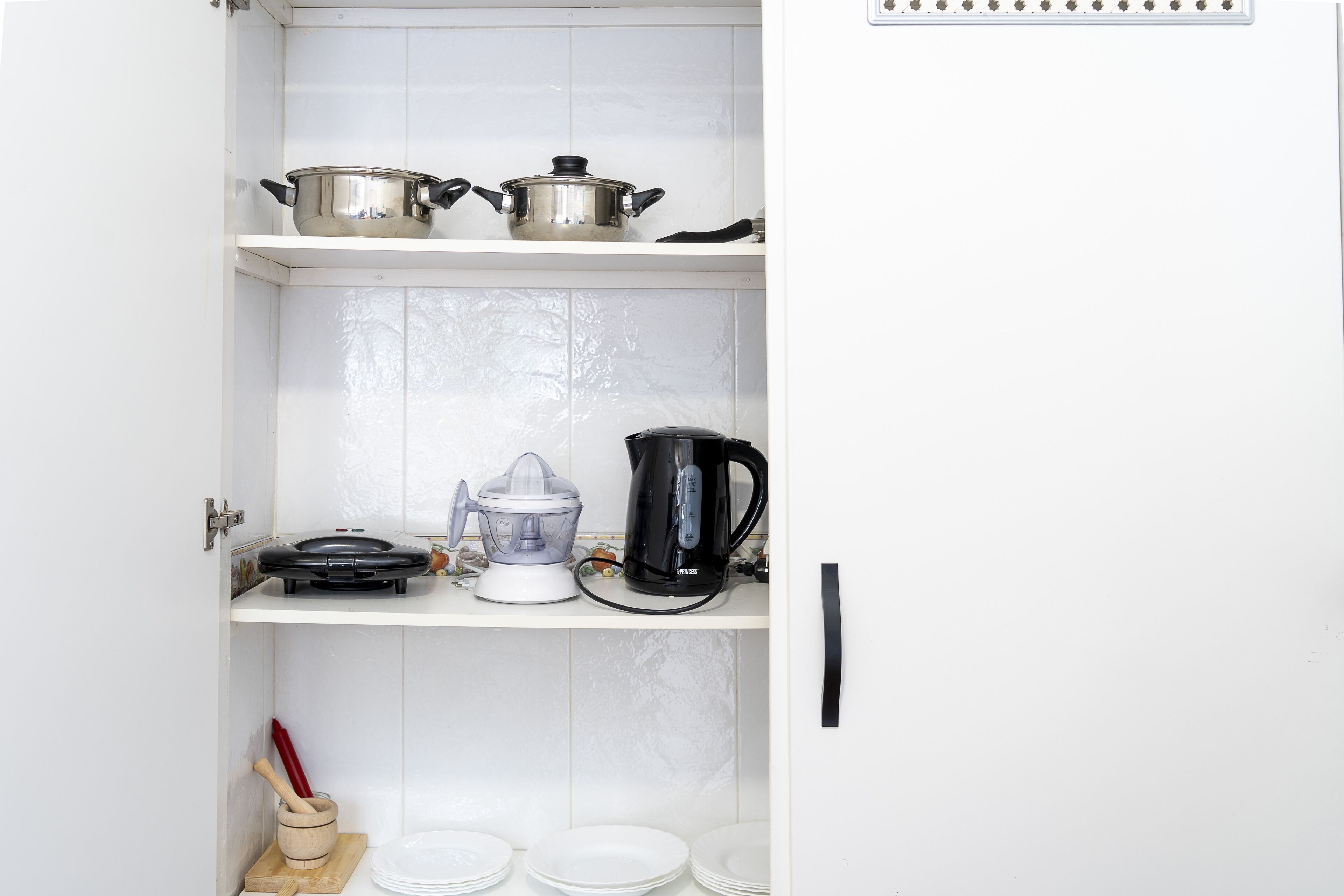 Une cuisine avec des meubles blancs, une machine à café, un mixeur et une casserole sur l’étagère supérieure.