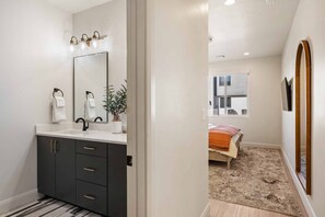 Un baño moderno con un espejo grande, muebles oscuros y una encimera blanca.