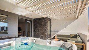 Et moderne udeområde med boblebad, stenvæg, træterrasse og et overdækket loungeområde.