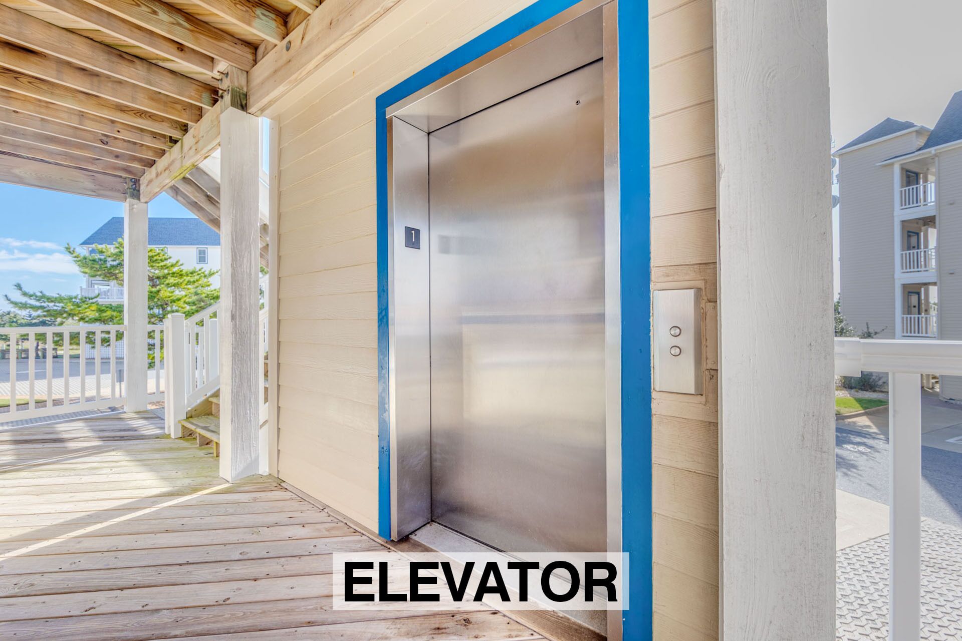 An elevator with a metallic finish, located in a building with a wooden exterior and a white picket fence.