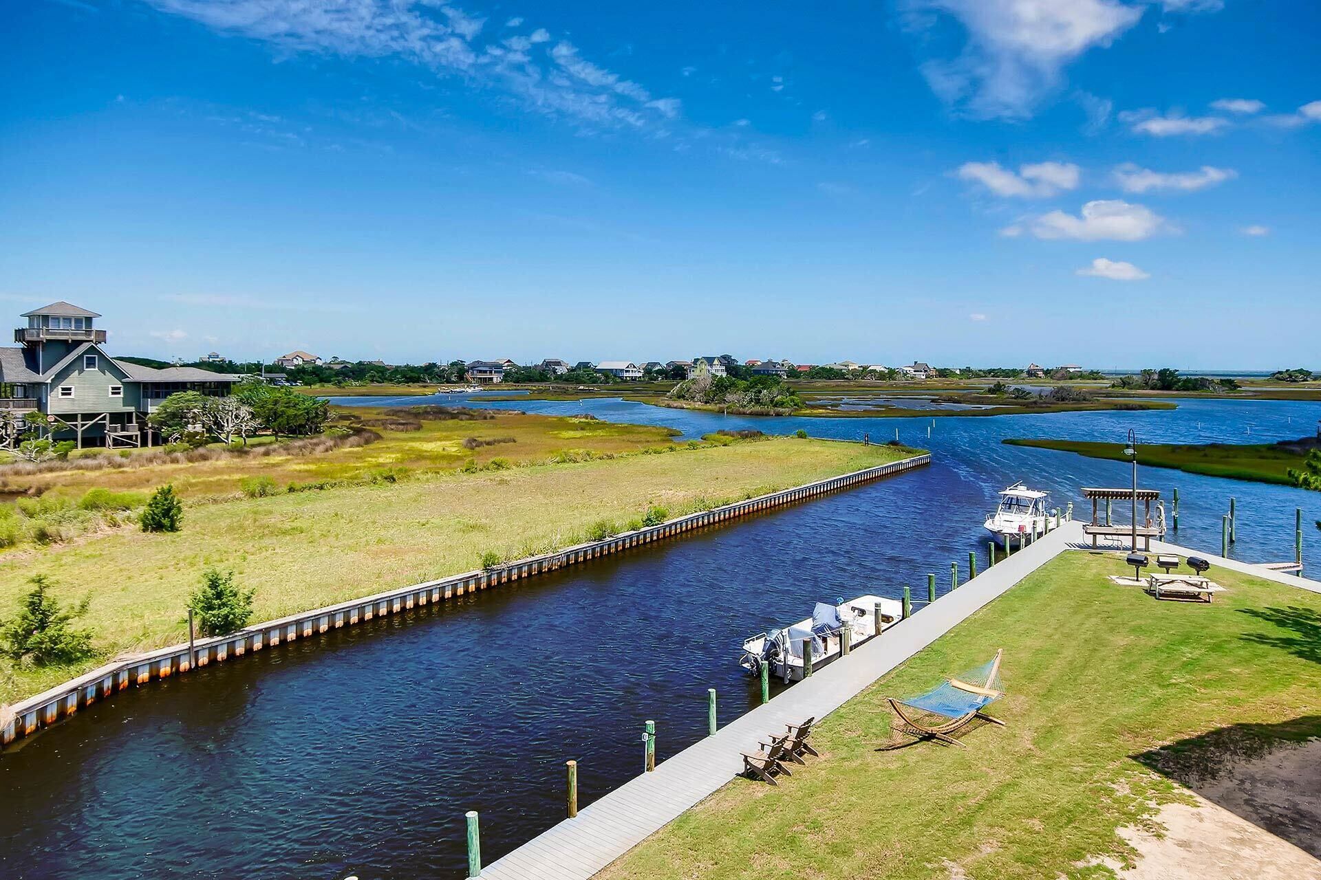 A river with a wooden walkway, a boat dock, and a grassy area with a hammock.