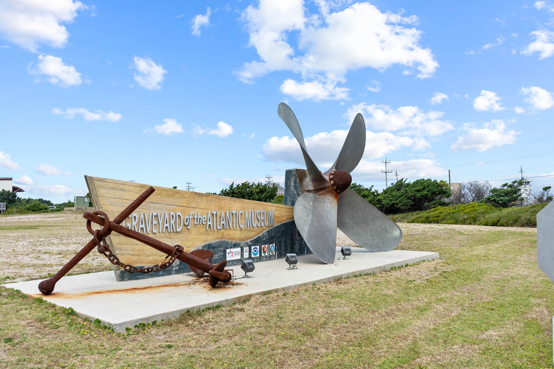 Eine Ausstellung maritimer Artefakte, darunter ein großes Anker und ein Schiffsrad, mit einem Schild im Hintergrund, auf dem ‚GRAVEYARD of the ATLANTIC MUSEUM‘ steht.