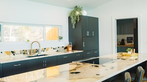 A modern kitchen with a marble countertop, dark cabinets, and a window providing natural light. - Sunrise+Sunset views - HotTub / Firepit / RecRoom / BBQ / Yoga studio /Treadmill (Central City)