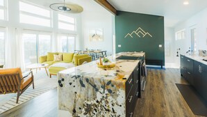A spacious living area with a large island, a dining area, and a kitchen with dark cabinetry. - Sunrise+Sunset views - HotTub / Firepit / RecRoom / BBQ / Yoga studio /Treadmill (Central City)
