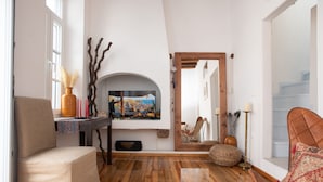 A cozy living room with a wooden floor, a beige armchair, a television, and a mirror reflecting the room.