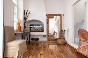 Una sala de estar acogedora con suelo de madera, un sillón color beige, un televisor y un espejo que refleja la habitación.