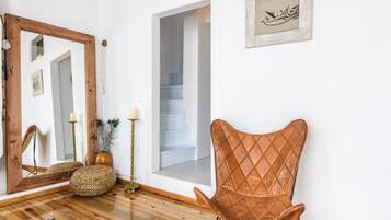 Una habitación con piso de madera, un sillón de cuero marrón, un espejo, un florero con plantas secas y un cuadro en la pared.